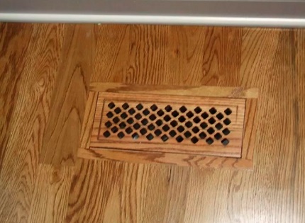 Rejilla de ventilación en el piso de una casa de madera.